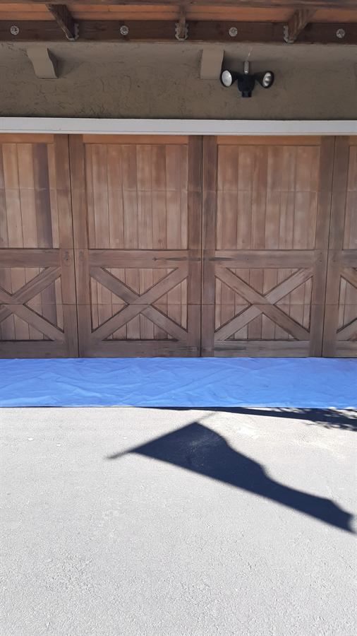 Weathered wood garage doors before refinishing, drop cloth laid out along the driveway