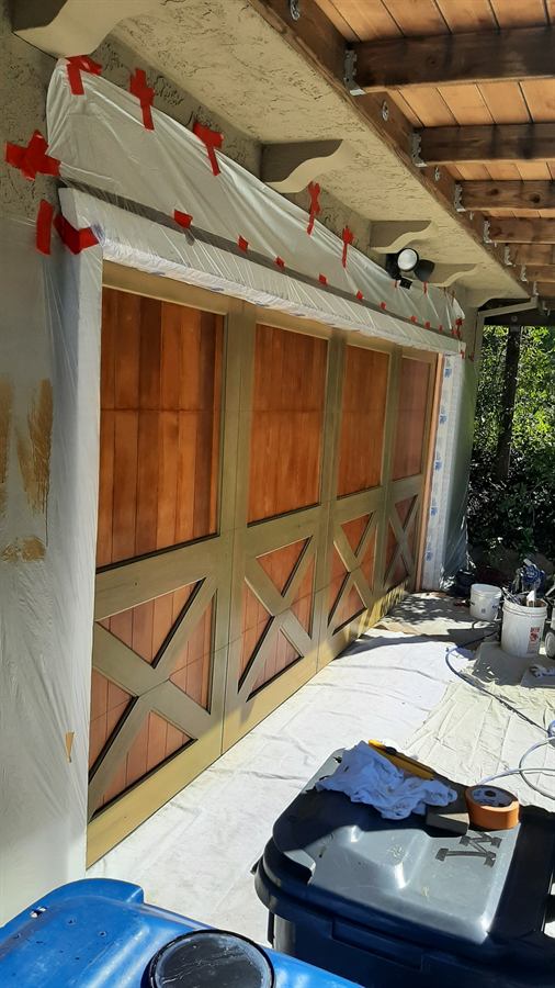 Garage doors masked off with plastic sheeting, freshly stained panels and painted trim