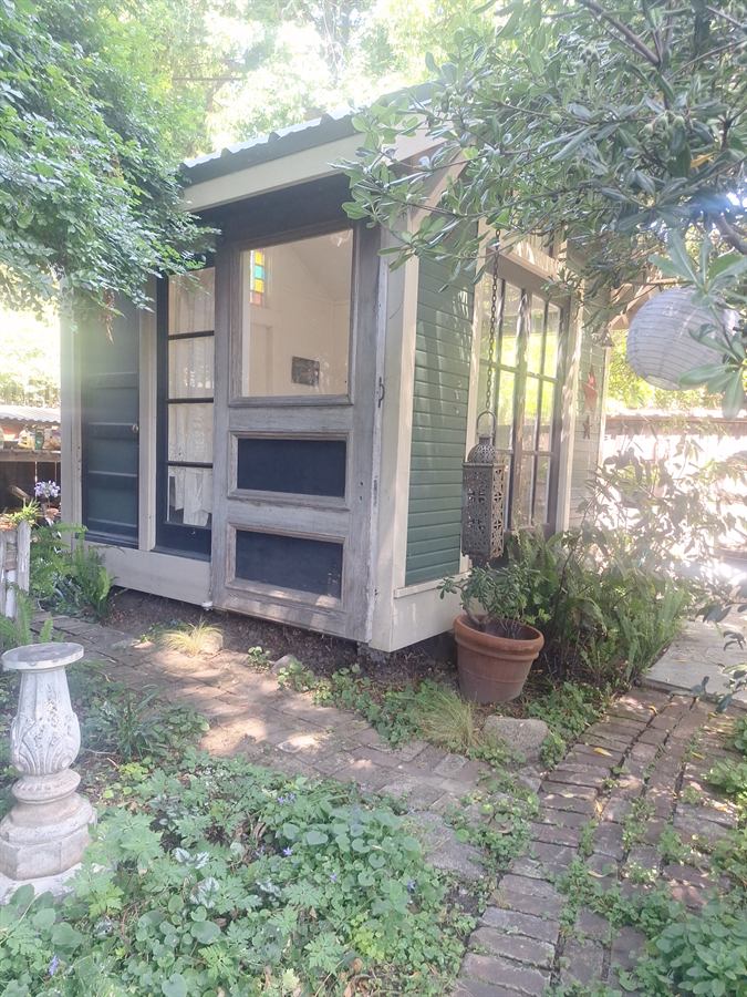 Garden cottage before repainting, with weathered cream siding and green shutters