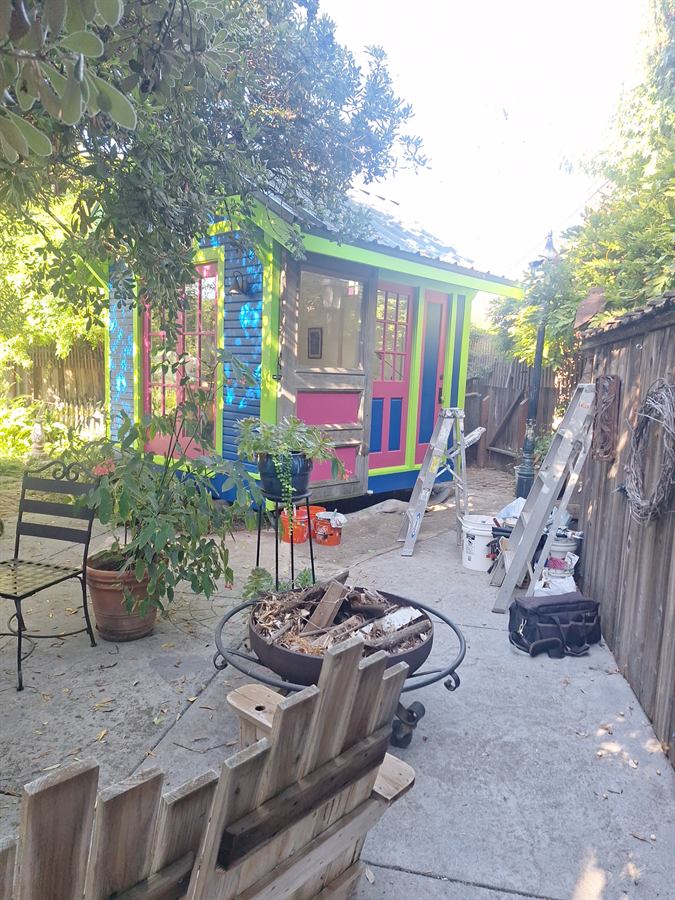 The same garden cottage repainted in blue, lime and magenta, with ladders and tools still on site
