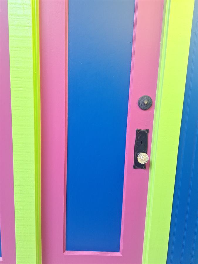 Close-up of a pink and blue painted door panel with an antique glass knob