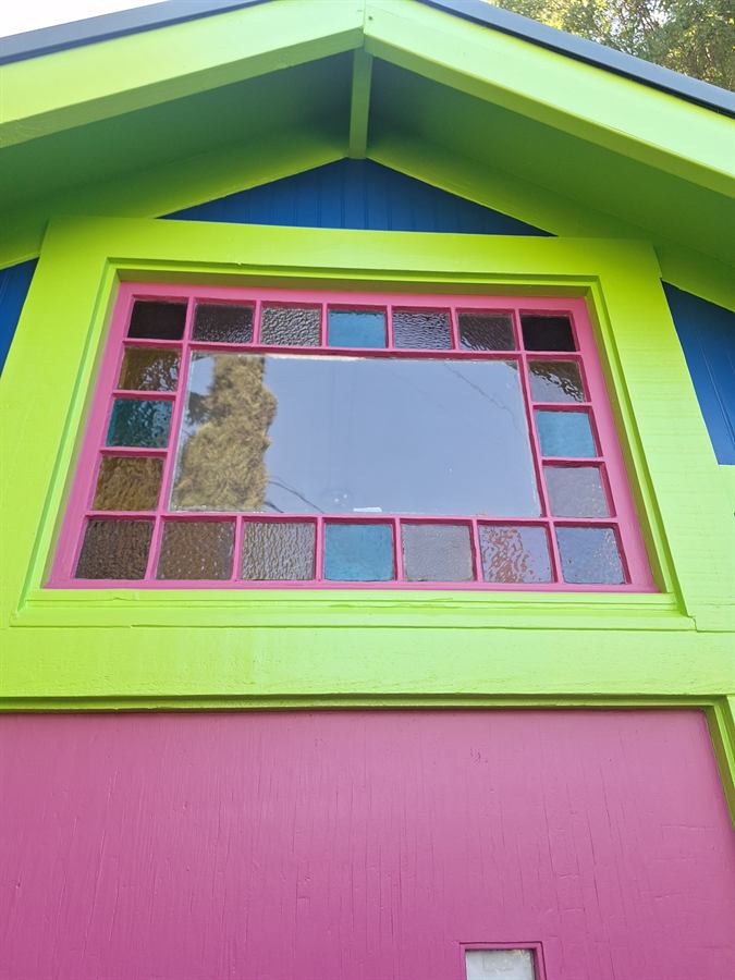 Painted gable end with a multi-pane leaded window in lime and magenta trim